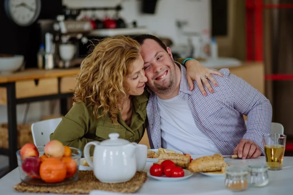 Happy disabled man sitting at table with support worker both smiling